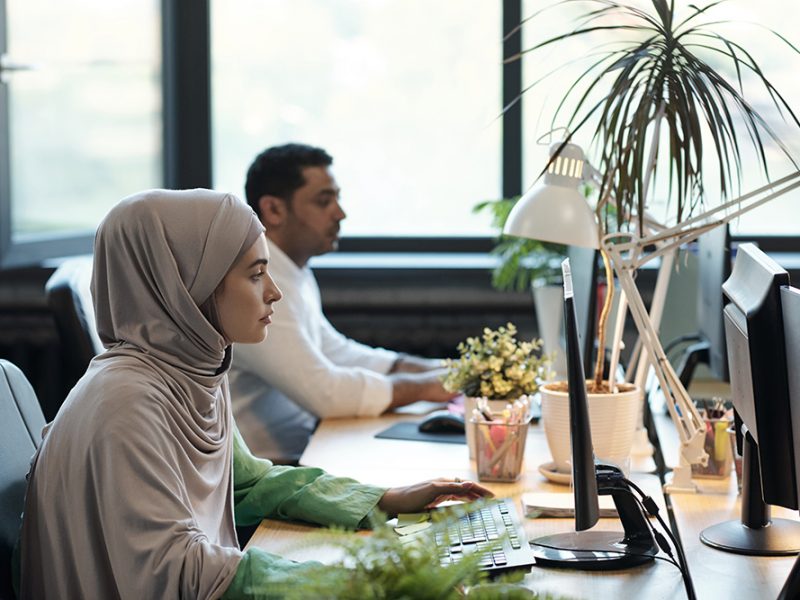 Young Muslim businesswoman in hijab and her male colleague computing by workplace